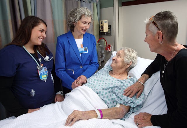 family members and a nurse comfort a patient in a hospital bed